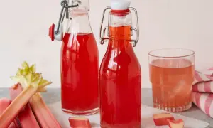 Zwei Flaschen mit leuchtend rotem Rhabarbersirup, ein Glas und frische Rhabarberstangen. Perfekt für ein erfrischendes Rhabarbersirup Rezept.