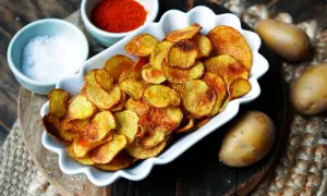 Knusprige, selbstgemachte Kartoffelchips, gewürzt mit Paprika und Salz, daneben rohe Kartoffeln. So einfach ist es, Chips selber machen!