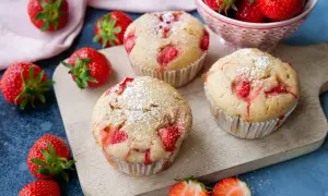 Saftige erdbeer muffins, bestäubt mit Puderzucker, liegen auf einem Holzbrett. Frische Erdbeeren umgeben die Leckereien.