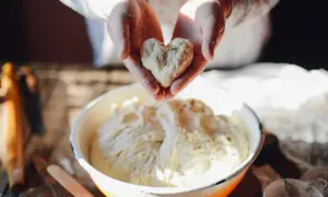 Hefeteig geht nicht auf? Ein Herz aus Teig in Händen über einer Schüssel voller Teig.