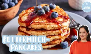 Fluffige pancakes mit Blaubeeren und Sirup, dazu eine lächelnde Frau.