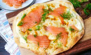 Flammkuchen mit Lachs, belegt mit zarten Lachsscheiben, cremiger Käsesauce und frischem Dill, garniert mit schwarzem Pfeffer.