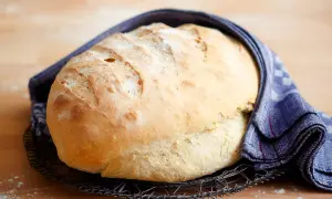 Frisch gebackenes Brot, das nach dem **Brot selber backen** auf einem Gitter abkühlt. Ein blau-weißes Tuch umhüllt es.