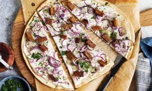 Flammkuchen vegetarisch mit roten Zwiebeln und knusprigen Tofuwürfeln, bestreut mit frischer Petersilie.