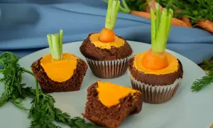 Schokoladen-Muffins mit orangefarbener Glasur und einem kleinen Karottenstück mit Grün als Osterdekoration.