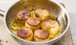 Sechs goldbraune Fondantkartoffeln in einer Pfanne mit Butter und Kräutern, bereit zum Servieren.