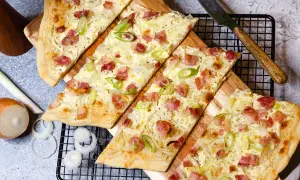 Drei knusprige Flammkuchen-Stücke mit Speck und Zwiebeln, bereit für ein köstliches Flammkuchen Rezept.