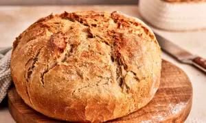 Ein frisch gebackenes, knuspriges Brot liegt auf einem Holzbrett. Dieses friss dich dumm Brot duftet herrlich und lädt zum Genießen ein.