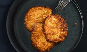 Drei goldbraune Kartoffelpuffer liegen auf einem dunklen Teller. Perfekt zubereitet mit dem Thermomix, sind sie ein Genuss.