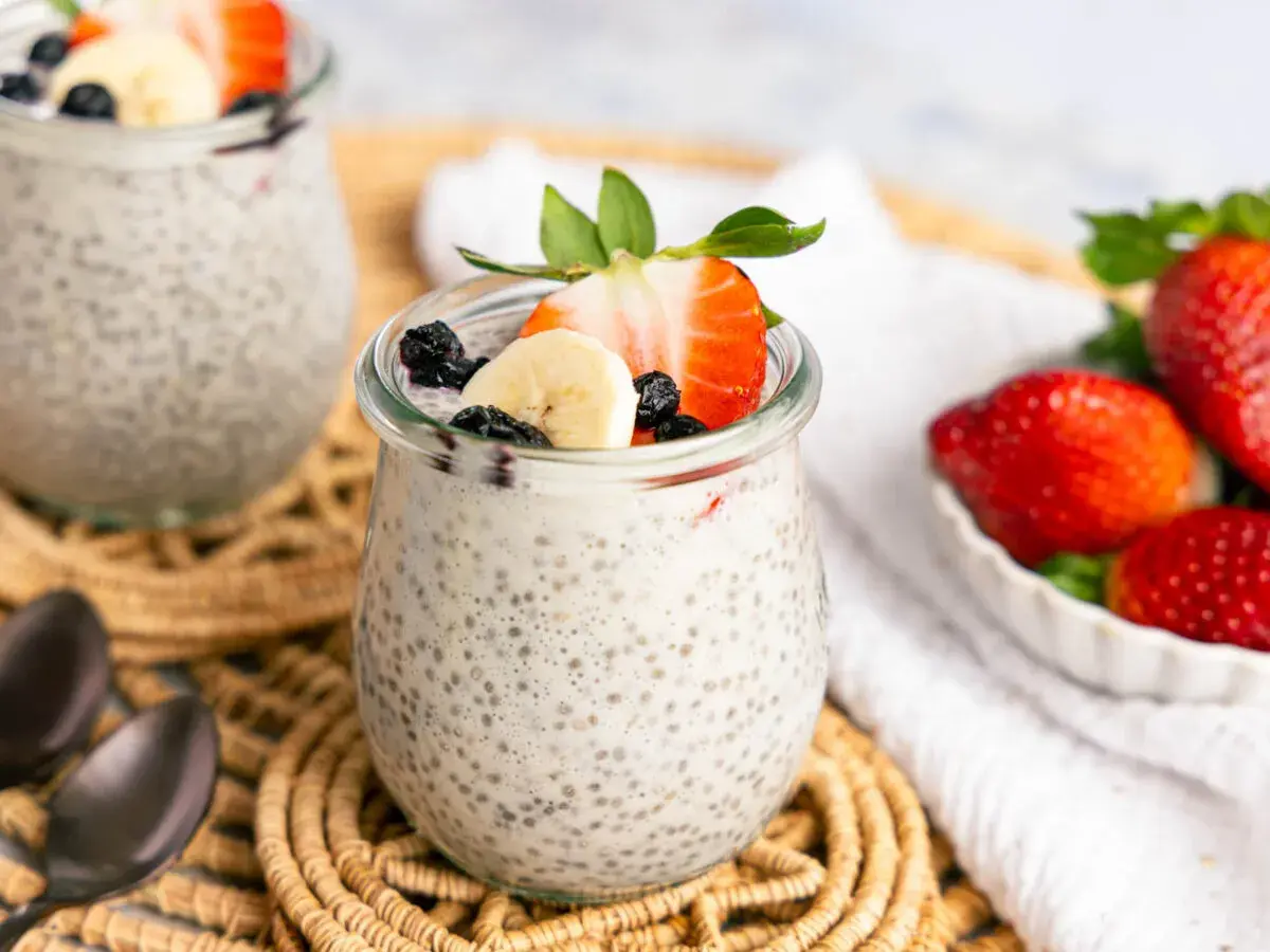 Zwei Gläser mit cremigem Chia Pudding, garniert mit Erdbeeren, Bananen und Blaubeeren. Ein gesunder Genuss!