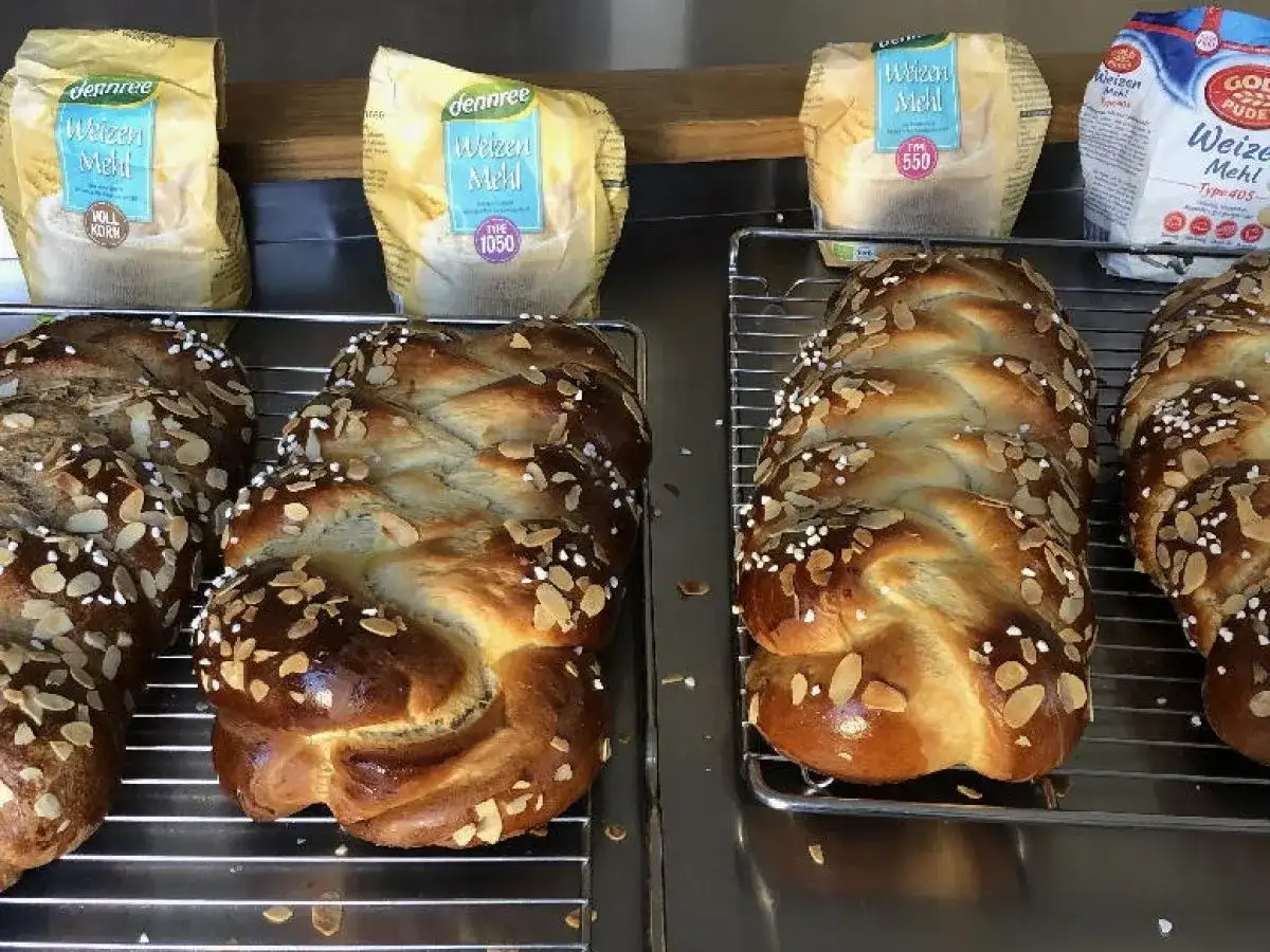 Frisch gebackene Hefezöpfe mit Mandelsplittern, bereit, um sie hefezopf frisch halten. Im Hintergrund Weizenmehl-Packungen.