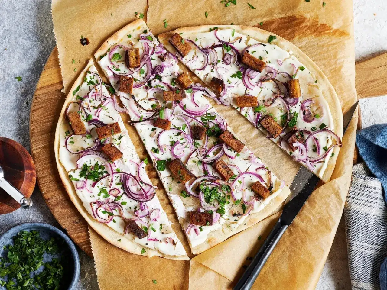 Flammkuchen vegetarisch mit roten Zwiebeln und knusprigen Tofuwürfeln, bestreut mit frischer Petersilie.