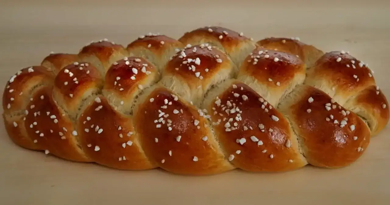 Ein goldbrauner, glänzender Hefezopf, bestreut mit Zuckerkristallen. Friedas genialer Hefezopf duftet verlockend und wartet darauf, angeschnitten zu werden.