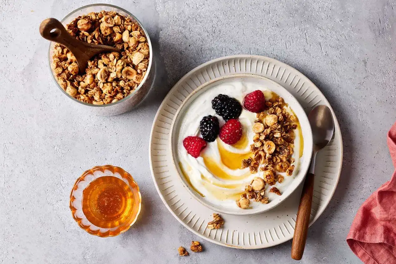 Schüssel mit Joghurt, Beeren und selbstgemachtem Granola, dazu Honig. Perfekt für ein gesundes Frühstück.