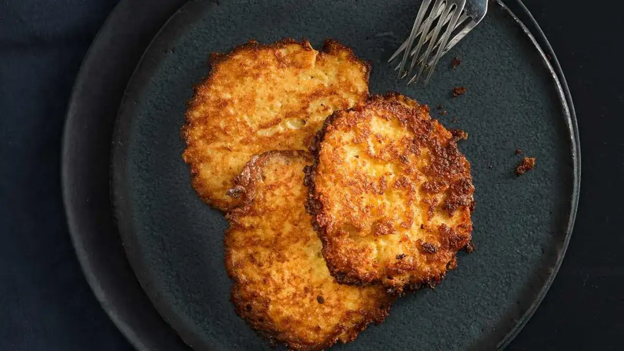 Drei goldbraune Kartoffelpuffer liegen auf einem dunklen Teller. Perfekt zubereitet mit dem Thermomix, sind sie ein Genuss.