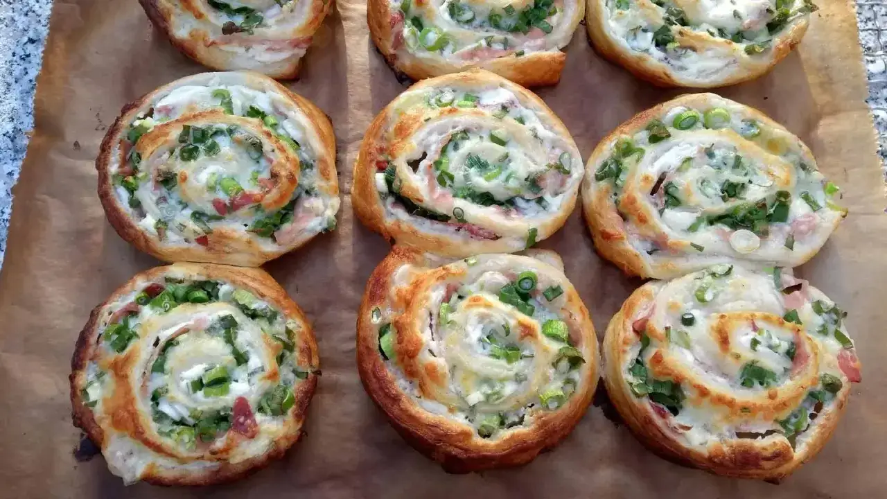 Leckere Flammkuchen Schnecken mit Speck und Frühlingszwiebeln, goldbraun gebacken auf Backpapier.