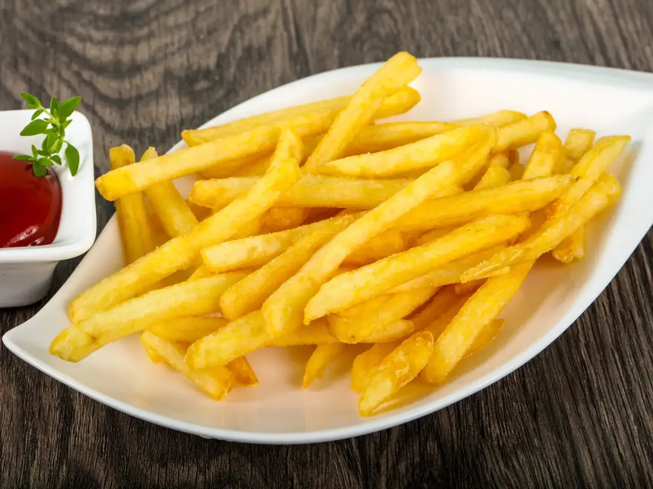 Goldgelbe, knusprige Pommes Frites auf einem weißen Teller, dazu eine kleine Schale Ketchup. Perfekt zum selber machen!