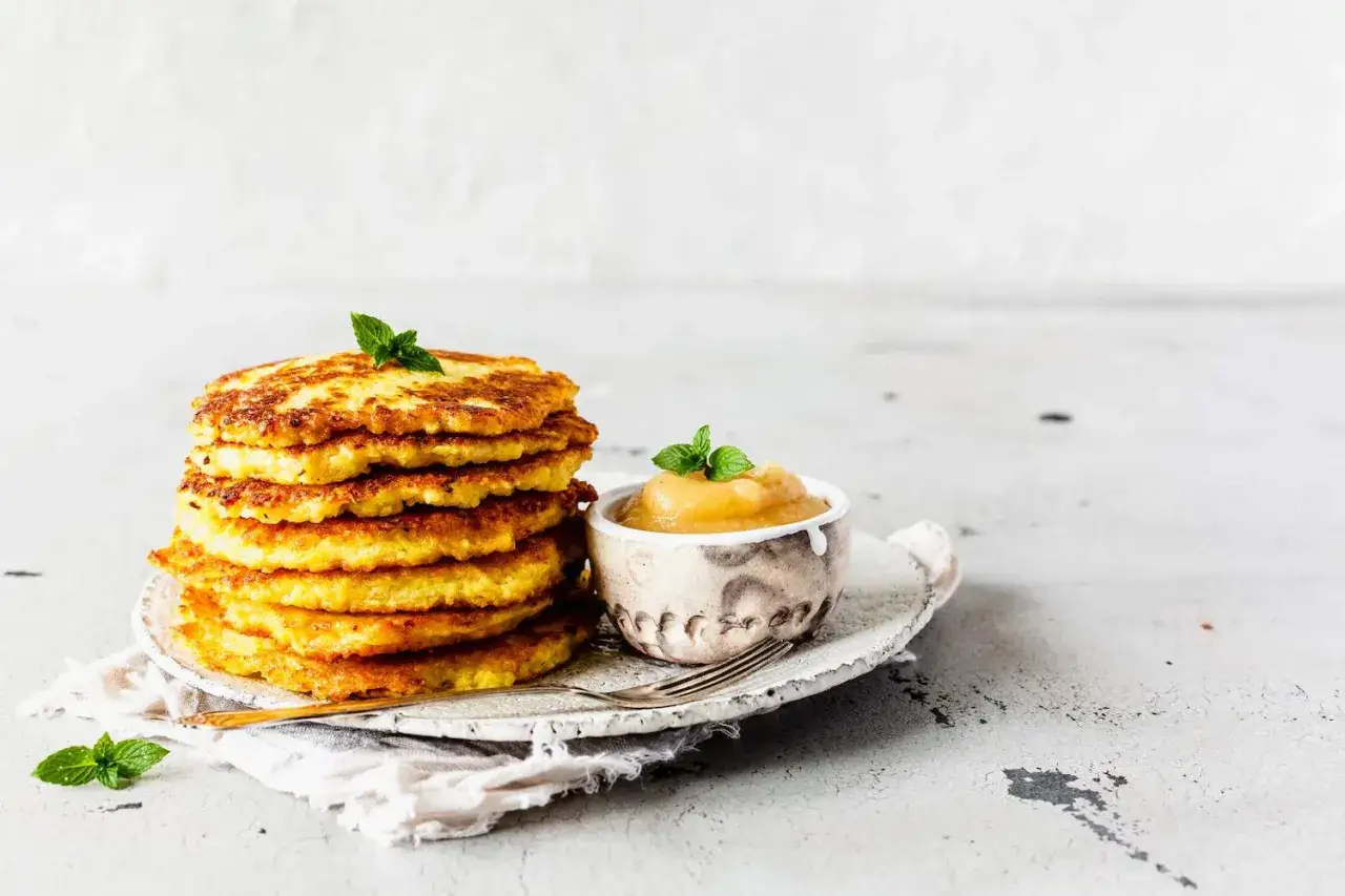 Stapel goldbrauner Kartoffelpuffer, frisch aus dem Thermomix, mit Apfelmus und Minze garniert.