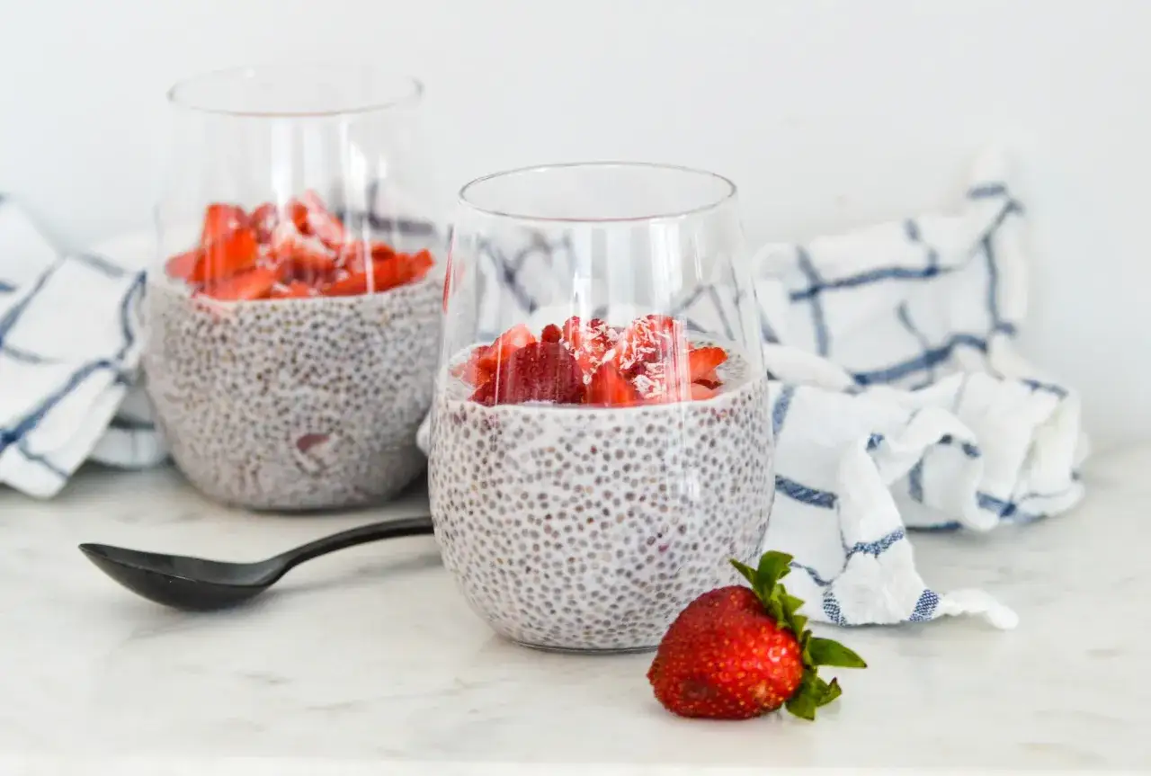 Zwei Gläser mit cremigem Chia Pudding, garniert mit frischen Erdbeeren und Kokosraspeln. Ein gesunder Genuss!