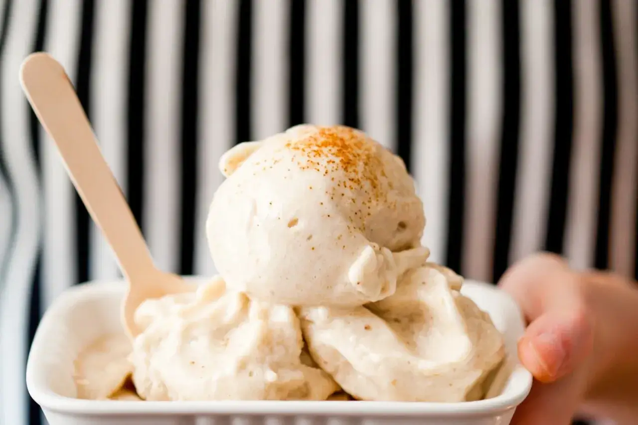 Cremiges Bananeneis, das man ganz einfach selber machen kann, in einer weißen Schale mit Holzlöffel. Mit Zimt bestreut.