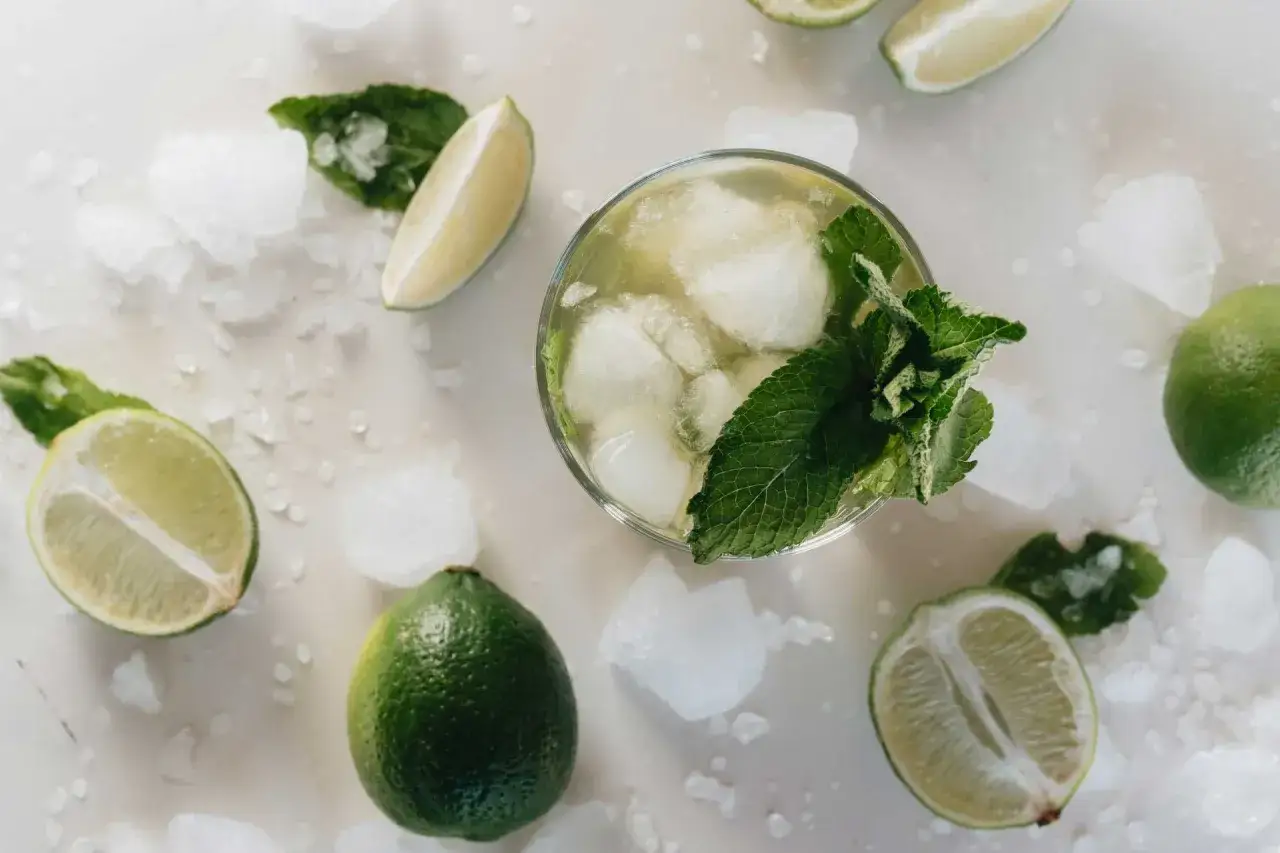 Erfrischendes Maibowle Rezept: Glas mit Eis, Minze und Limettenspalten, umgeben von ganzen und halbierten Limetten und zerstoßenem Eis.