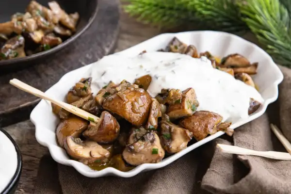 Gebratene Champignons mit Kräuterquark, wie vom Weihnachtsmarkt, auf einem weißen Teller mit Holzspießen.