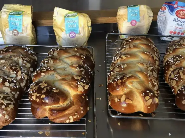 Frisch gebackene Hefezöpfe mit Mandelsplittern, bereit, um sie hefezopf frisch halten. Im Hintergrund Weizenmehl-Packungen.