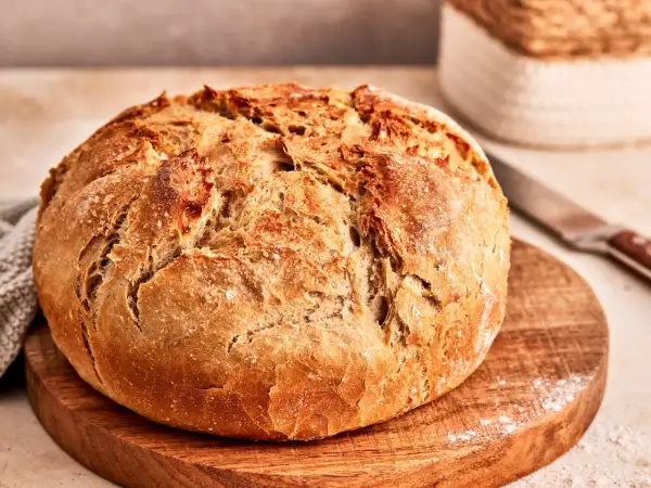 Ein frisch gebackenes, knuspriges Brot liegt auf einem Holzbrett. Dieses friss dich dumm Brot duftet herrlich und lädt zum Genießen ein.