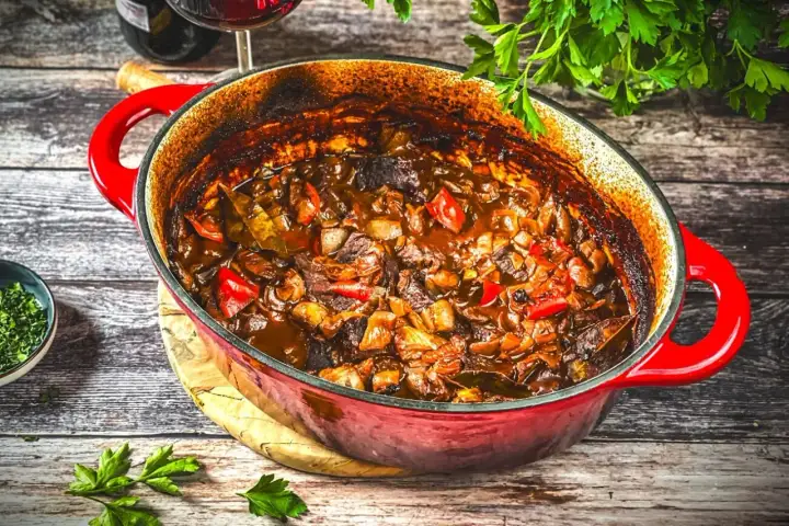 Herzhaftes Kalbsgulasch im roten Bräter, ein köstliches Rezept mit Paprika und Zwiebeln, bereit zum Servieren.