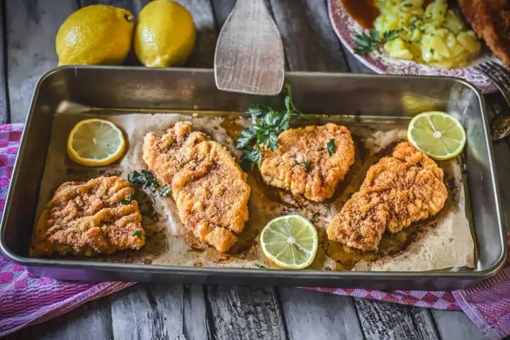 Vier goldbraune Schnitzel im Backofen, garniert mit Petersilie und Zitronenscheiben. Ein Genuss für Augen und Gaumen!
